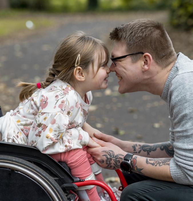 Little girl in wheelchair with her dad smiling